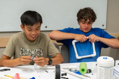 Two students smile as they build a structure with PVC pipe and pool noodle.